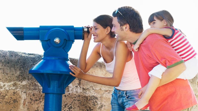 father and two daughters looking through telescope at landscape