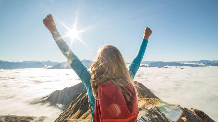 girl raises hands triumphantly at top of mountain