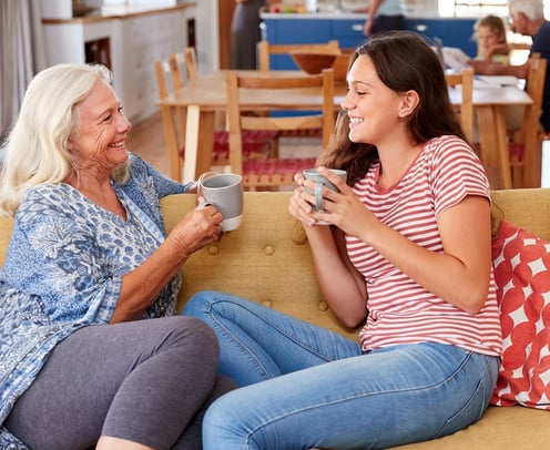 teen girl on couch with senior woman drinking coffee together