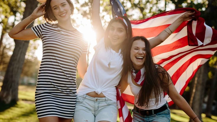happy American teenage girls in front of an American flag