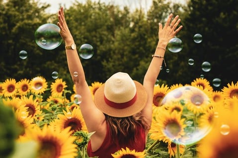 happy girl raising both arms to the sky in a sunflower field to illustrate cultural adaptation and overcoming culture shock