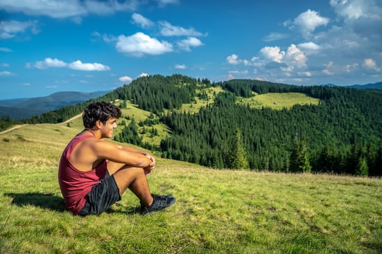 teen boy sitting in grass enjoying beautiful mountain view