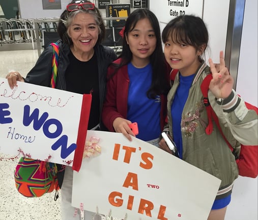 host mother greets two asian teenagers at airport