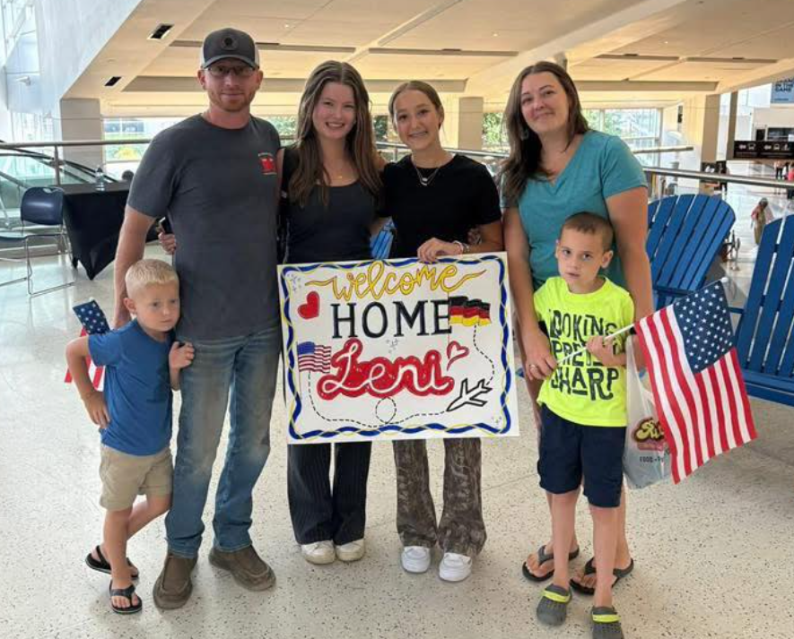family with welcome sign and flag at airport
