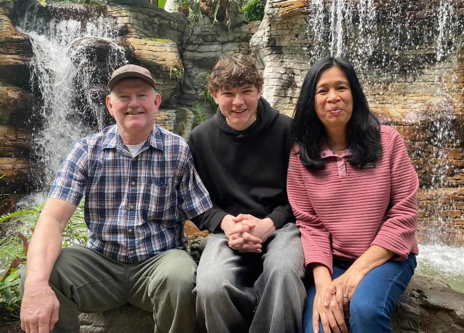 host parents and boy in front of waterfall