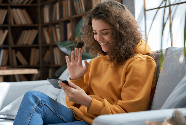 young woman waving to phone and smiling