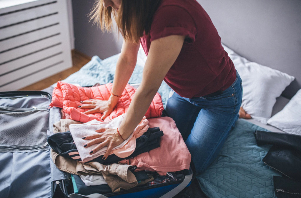 girl shoving clothes in overfull suitcase