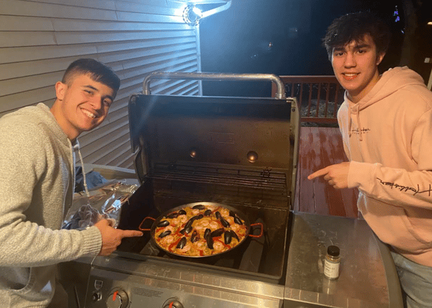 two teen boys making paella on a grill