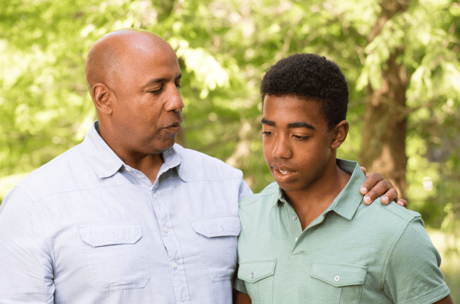 father with arm around son's shoulders talking