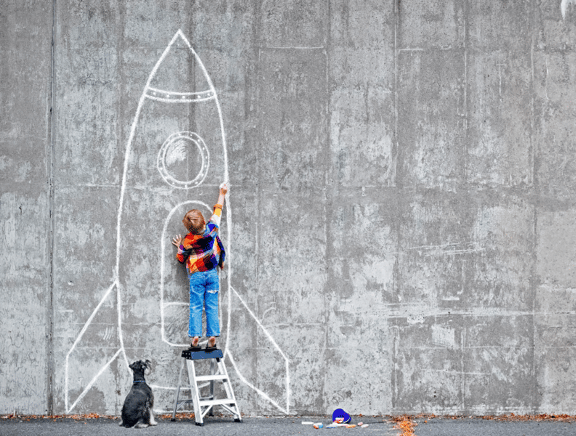 small boy drawing rocket on wall with chalk