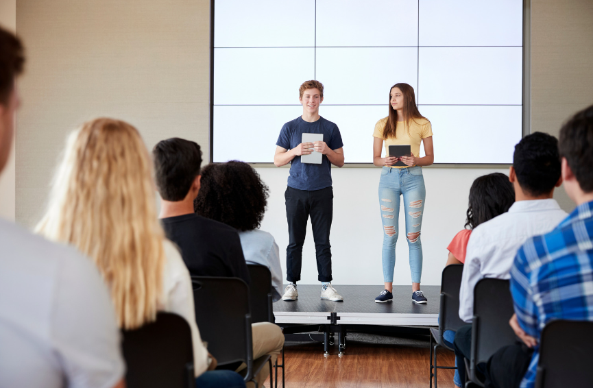 two teens speaking in front of audience