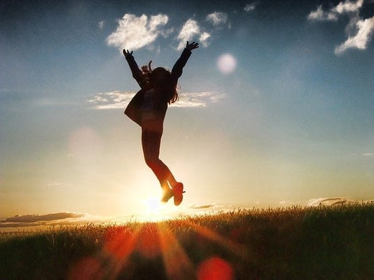 a teenage girl jumping in the air triumphantly in the sunset