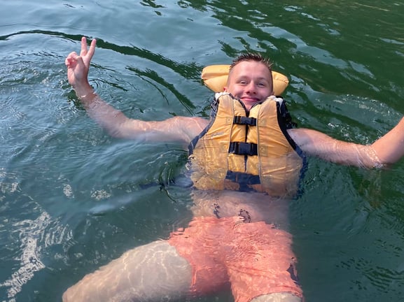 Nicolas floating in life jacket with peace sign