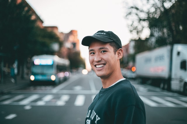 Teenage boy from South Korea smiling, wearing baseball cap and standing in the street