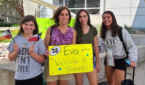 mother and two daughters welcome exchange student with a yellow welcome sign