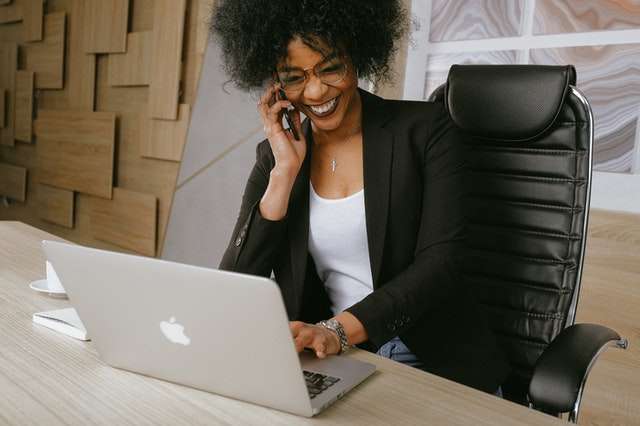 a woman of color smiling and talking on the phone while working on computer