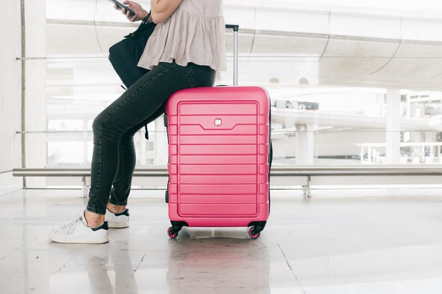 teenage girl sitting on her pink suitcase looking at her phone