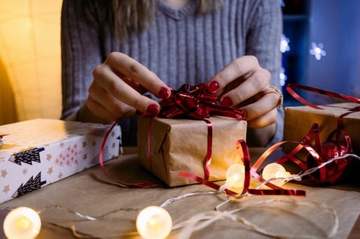 girl wrapping a package in brown paper with red ribbon and bow