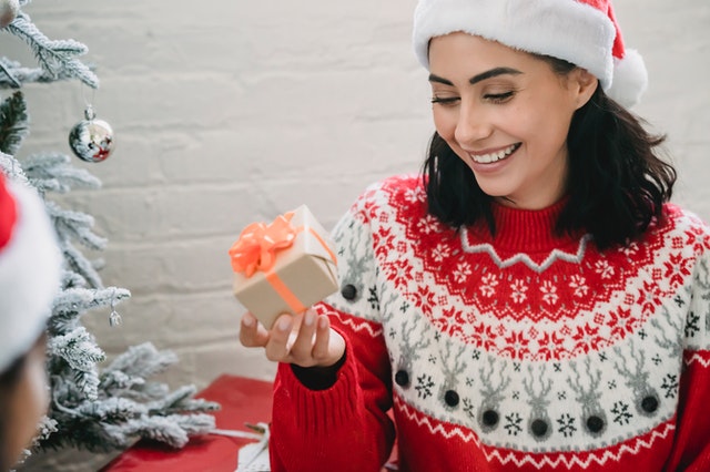 smiling girl holds Christmas gift sitting by tree