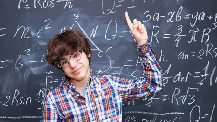 smiling teenage boy pointing at math on blackboard