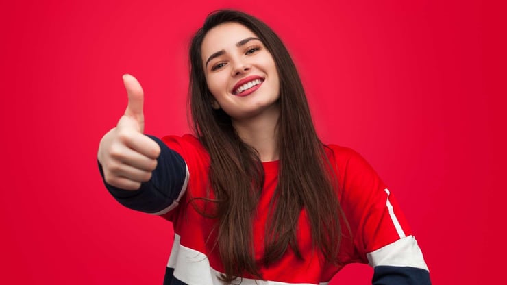 smiling teenage girl showing thumb up against a red background