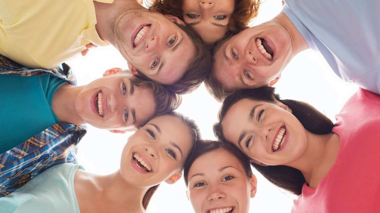 smiling teenagers with heads together in a circle