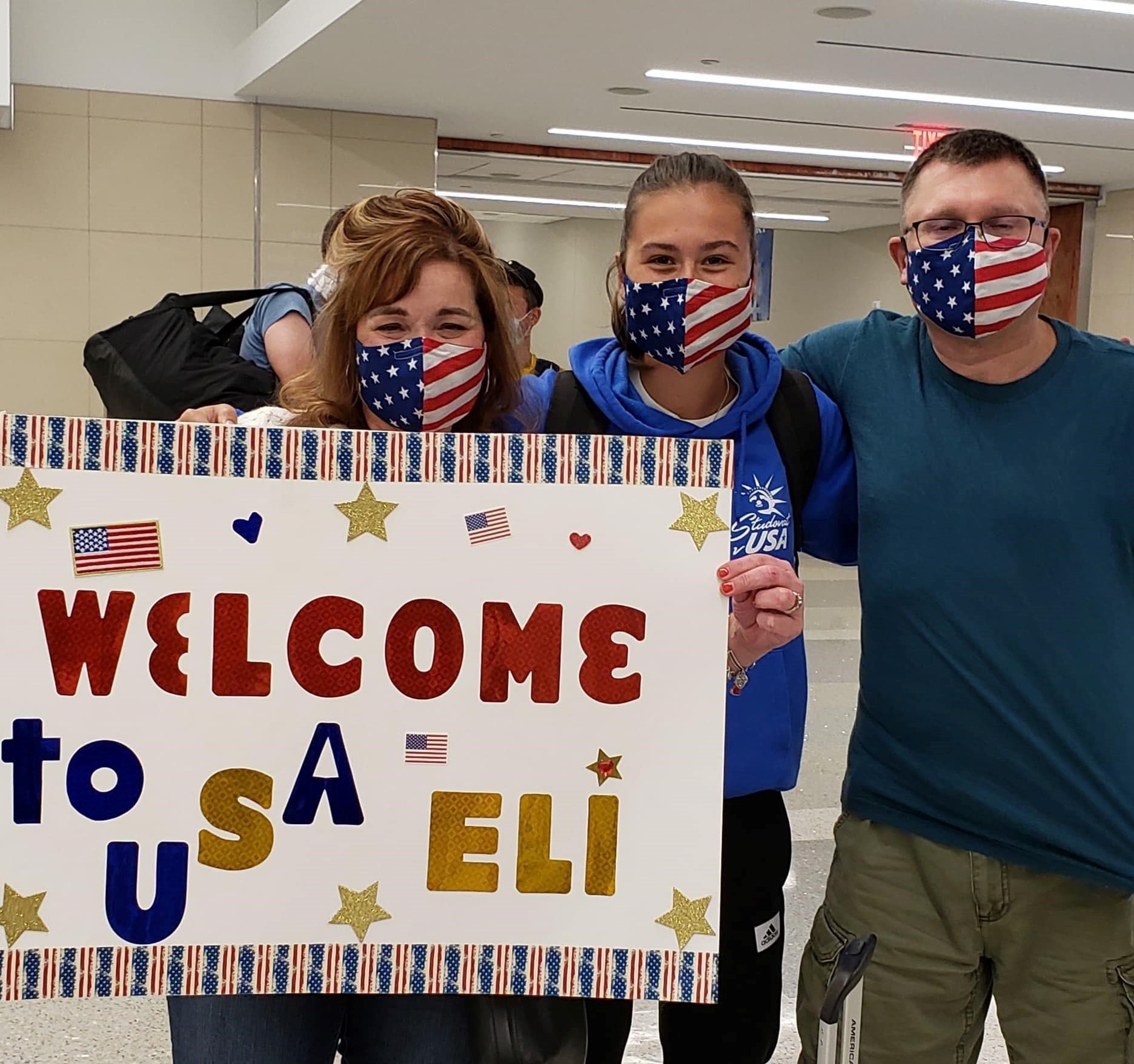 family wearing masks at the airport holding welcome sign for exchange student