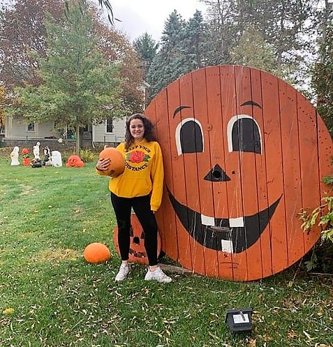 girl holding pumpkin standing with large wooden jack-o-lantern