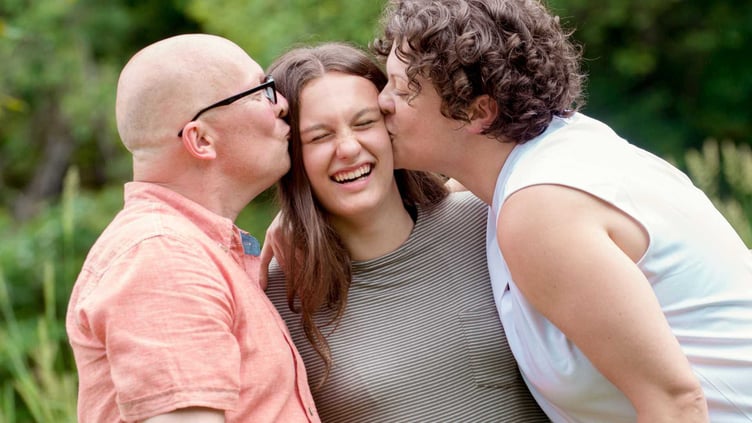 teen girl smiles as mother and father kiss her head
