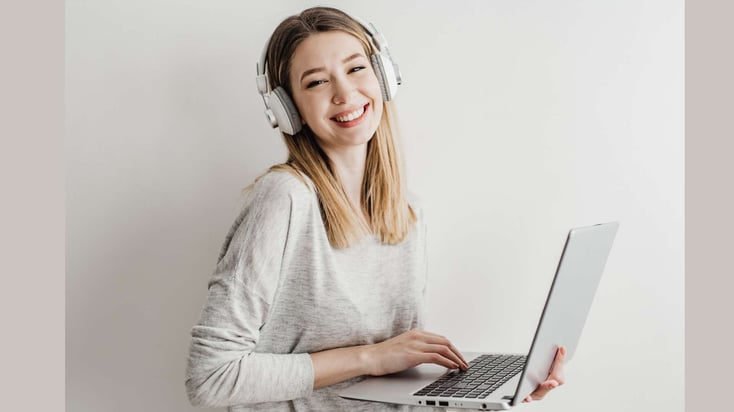 teen girl wearing headphones and standing with computer and smiling