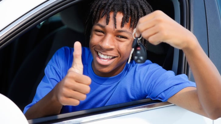 teenage boy in drivers seat smiling with thumb up
