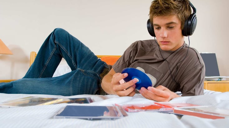 teenage boy in his room with headphones on and a cd in his hand