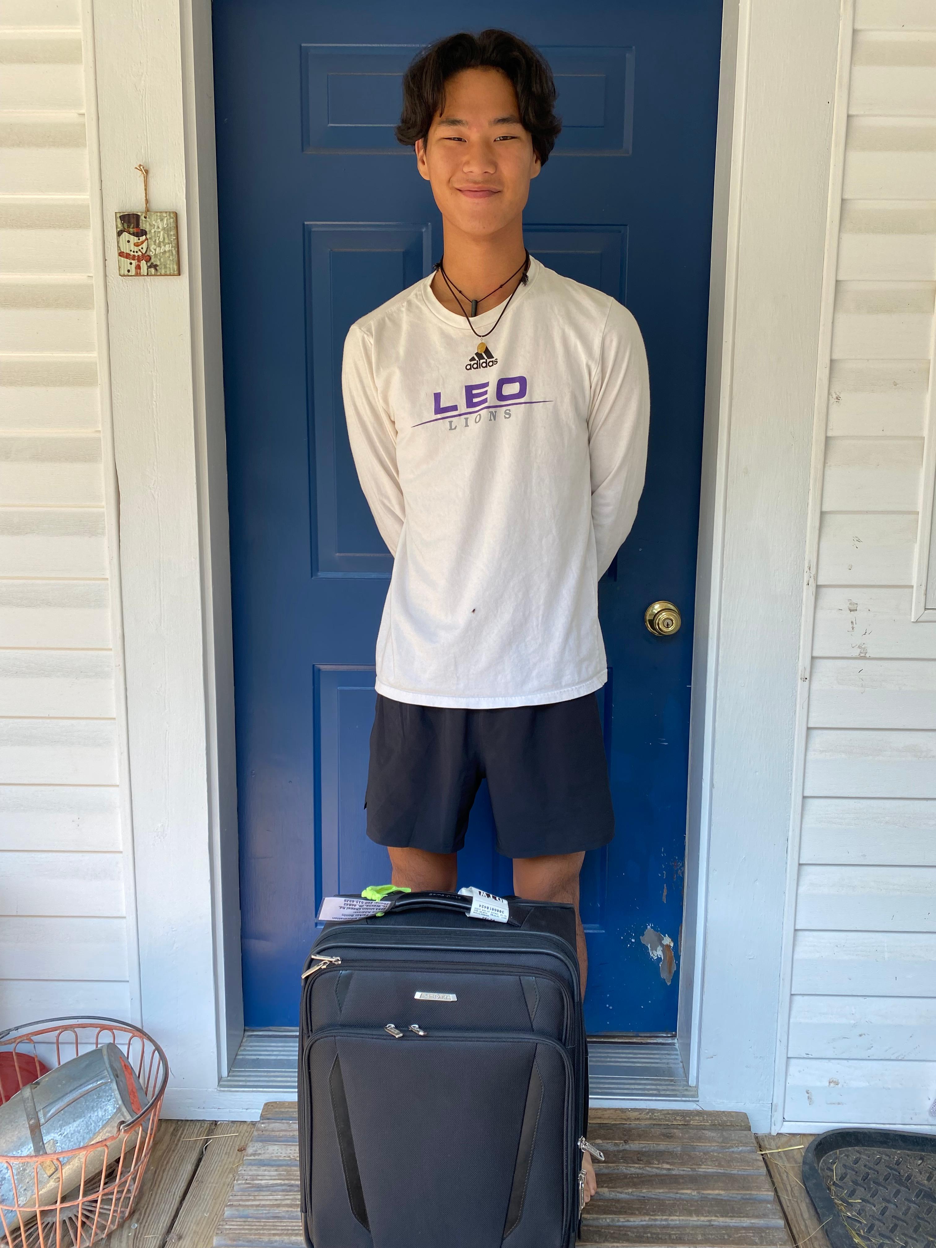 teenage boy with suitcase standing in front of door