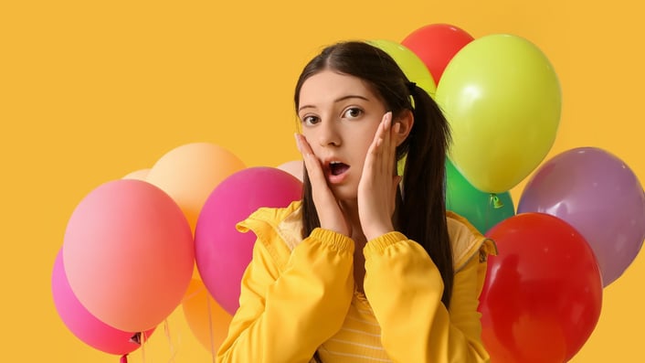 teenage girl looking surprised with balloons in the background
