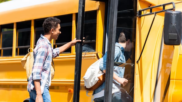 teenagers boarding a yellow schoolbus