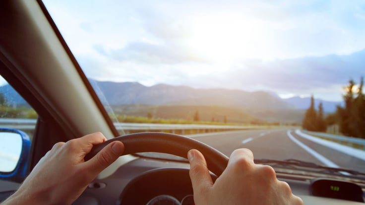 two hands on steering wheel driving down the road