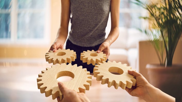 two people holding large wooden gears and matching them up