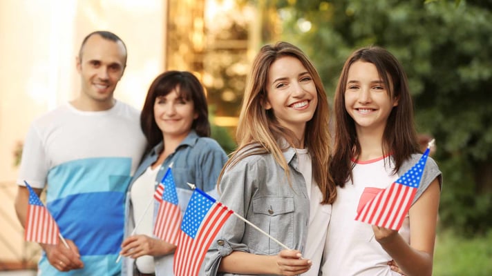 two teenage girls with american flags and parents in the background