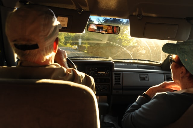 an older man driving a car with a female passenger