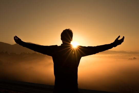 young man standing with arms wide open looking at the sunset