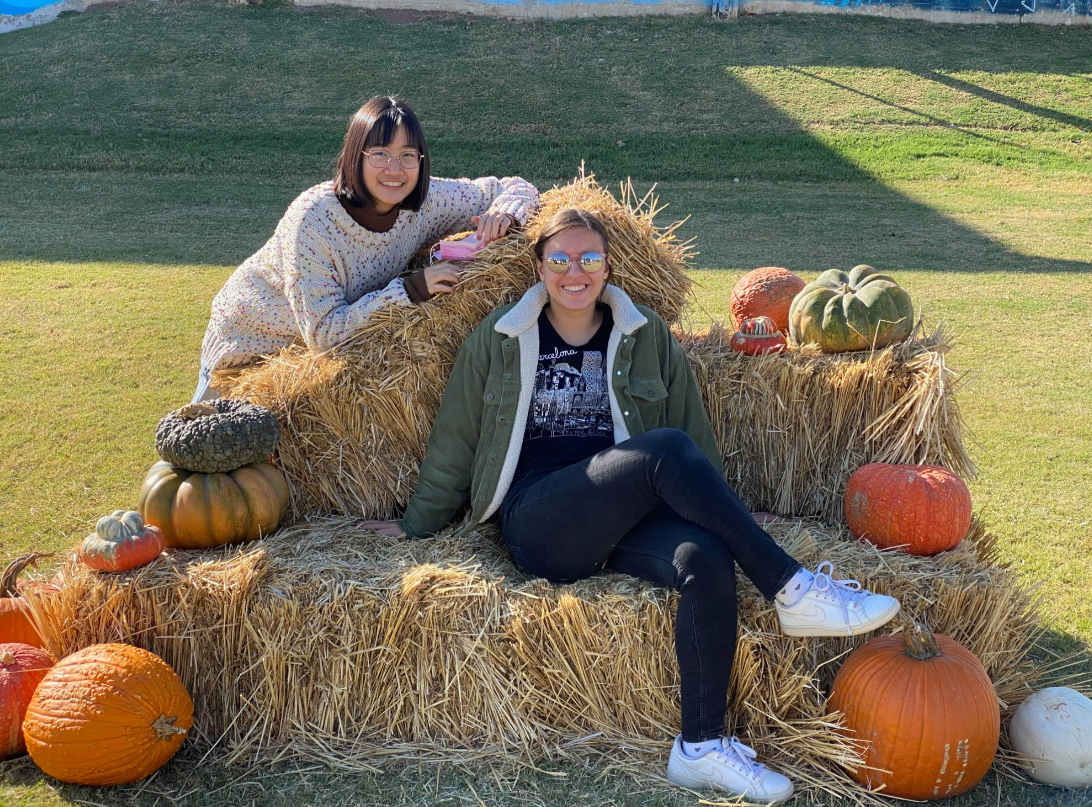 two teen girls sitting on hay bales with pumpkins