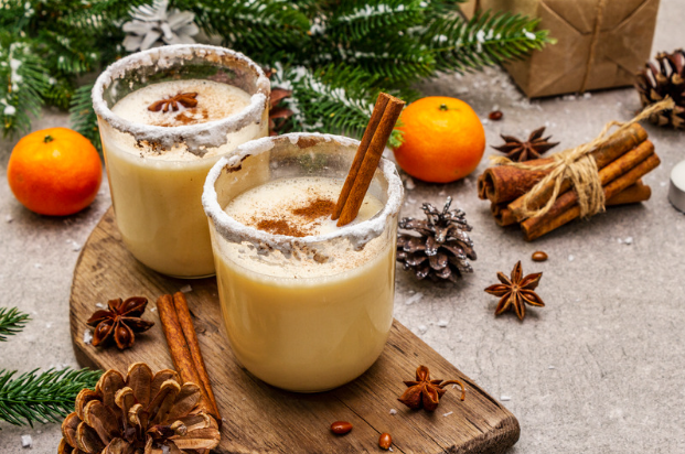 two glasses of eggnog displayed with cinnamon and orange