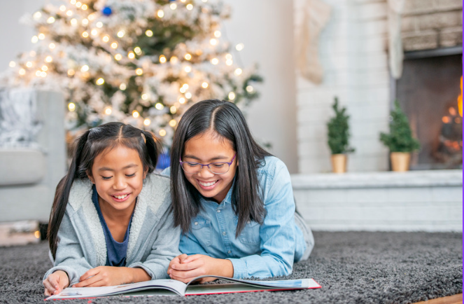 teen and younger girl reading in front of Christmas tree