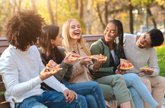 five teens eating pizza in a park